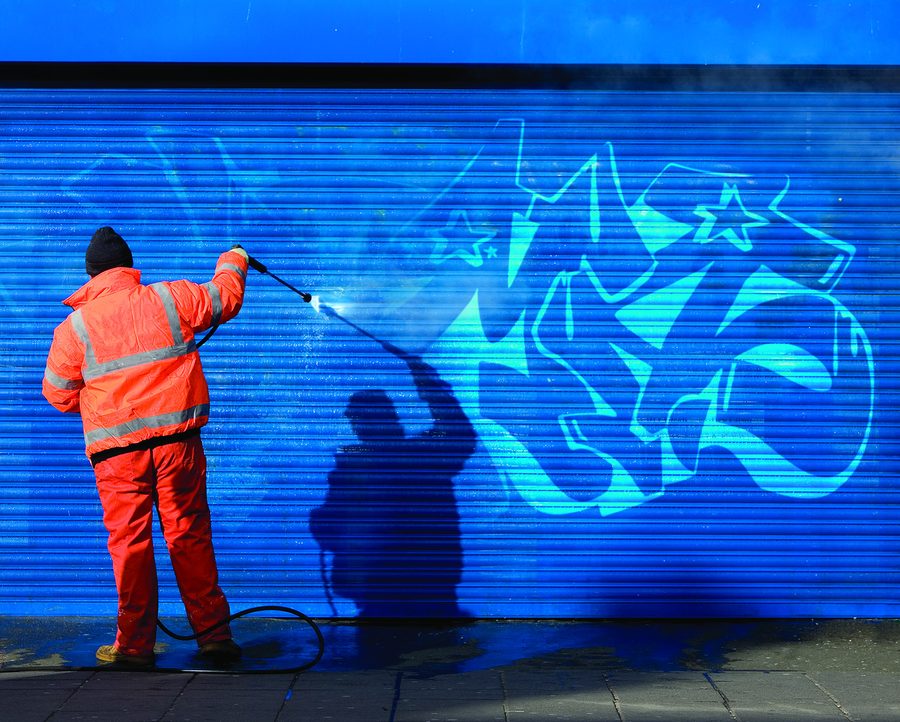 A worker cleaning graffiti from a blue shutter
